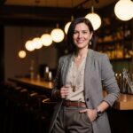 Stylová osoba slaví významné narozeniny v moderním baru s teplým osvětlením a dřevěným pultem.