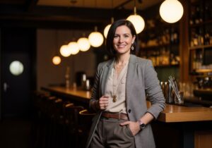 Stylová osoba slaví významné narozeniny v moderním baru s teplým osvětlením a dřevěným pultem.